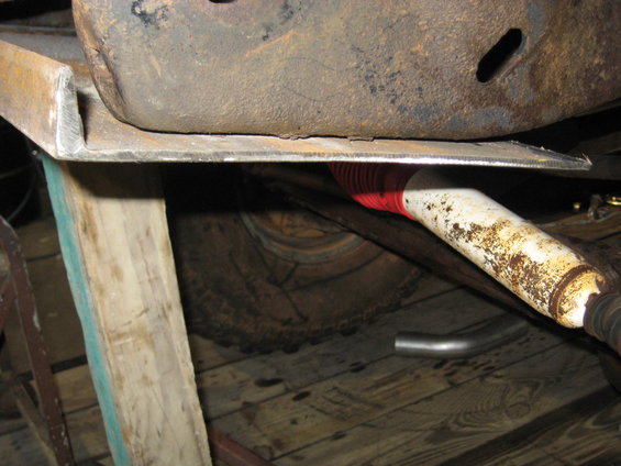 Close-up of vehicle underbody showing a rusty shock absorber with red bellows, exhaust pipe, and part of a tire