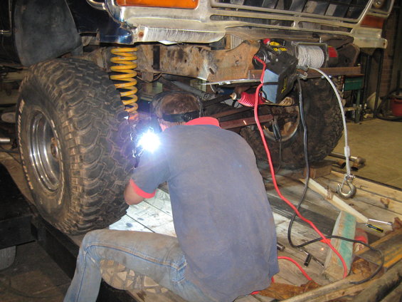 guy welding the frame of a large off-road vehicle, near the front tire and suspension
