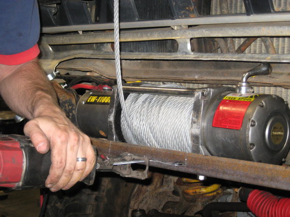 Winch being installed on a vehicle, showing the winch drum, cable, and a person's hands