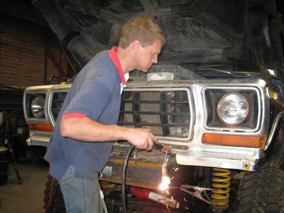 1978 Ford Bronco front end with a man welding the bumper, yellow springs visible