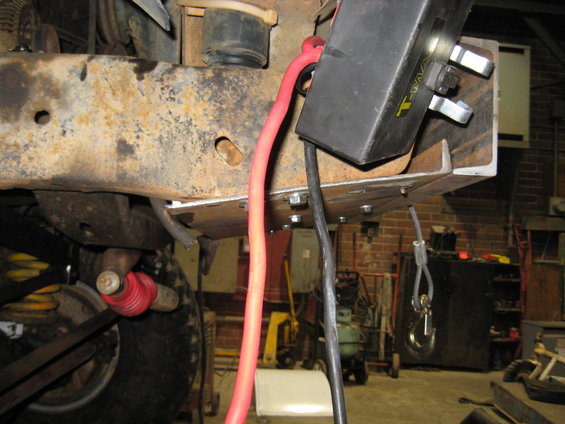 Winch mounting bracket bolted to rusty frame, with red and black cables attached