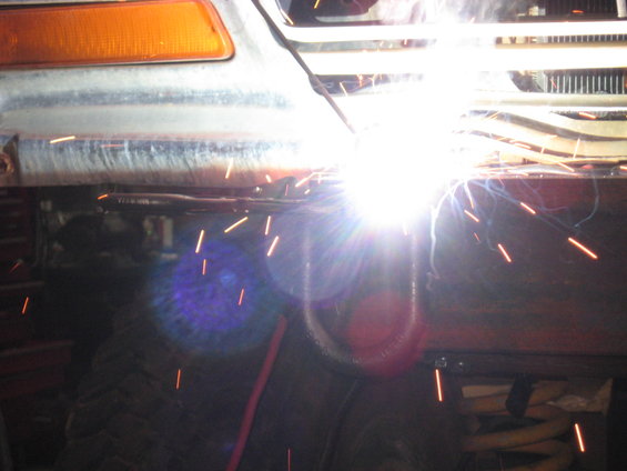 Welding sparks fly near orange turn signal and grille of a vehicle