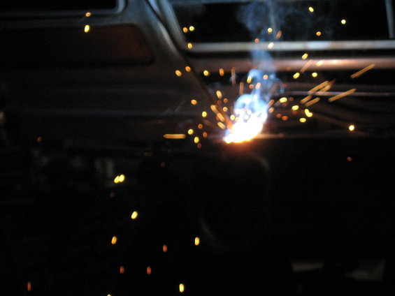 Bright welding sparks fly against a dark, out-of-focus background