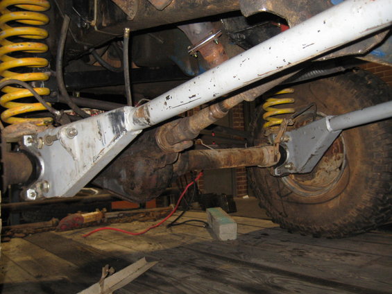 Undercarriage view showing suspension components, driveshaft, and tire. Yellow springs are visible