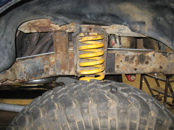 Close-up of rusty suspension with yellow coil spring and large tire