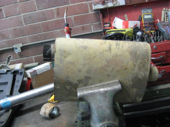 Yellowish exhaust pipe section held in a vise, with a metal pipe extending to the left