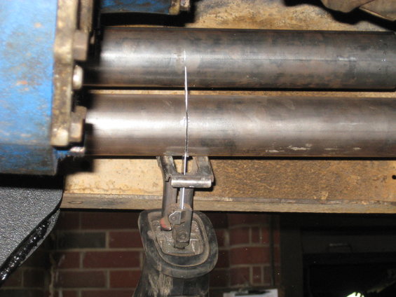Reciprocating saw blade cutting through a metal pipe held by rollers