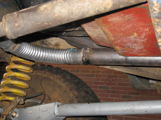 Close-up of flexible exhaust pipe and yellow coil spring under a vehicle