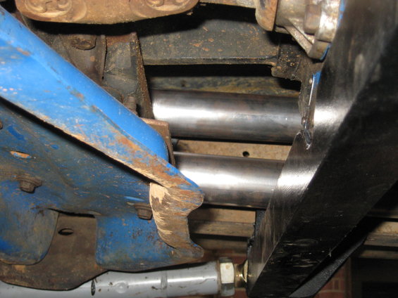 Underside view of a vehicle's suspension components, showing blue painted metal, rusty brackets, and shiny metal pipes