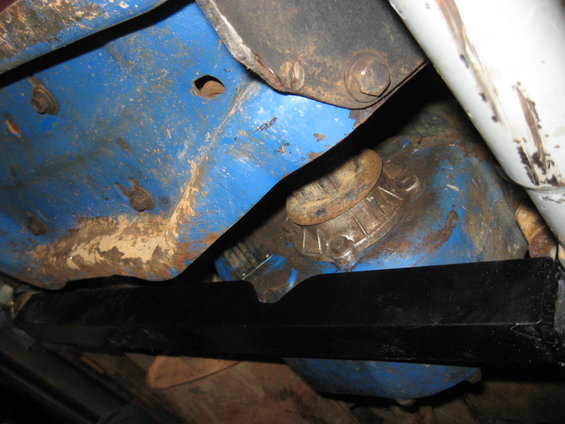 Underside of a vehicle with blue painted components, black crossmember, and white shock absorber