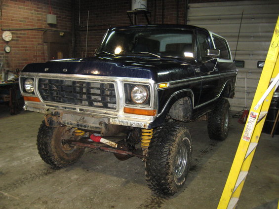 Dark blue 1978 Ford Bronco with lifted suspension and off-road tires in a garage