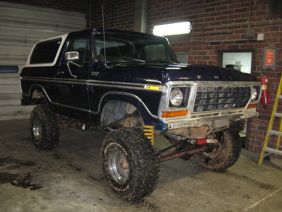 Dark blue 1978 Ford Bronco with a white hardtop, lifted with large tires, viewed from the front three-quarter angle