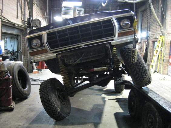 Ford F-Series truck on a lift, front end visible. It has a large grille and off-road tires
