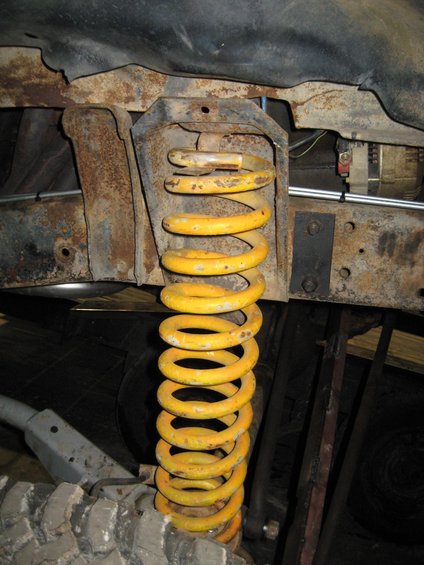 Close-up of a yellow suspension coil spring attached to rusty vehicle frame