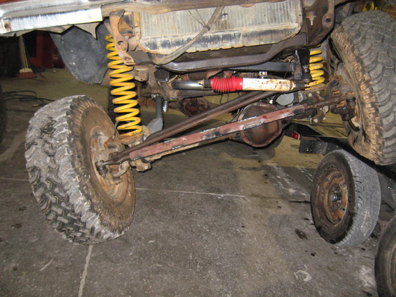 close-up of front suspension and drivetrain of an off-road vehicle, showing large tires, yellow springs, and red-and-white shock absorber