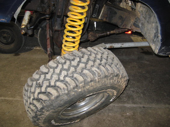 Close-up of a large off-road tire with BFGoodrich lettering, showing suspension components and yellow coil spring