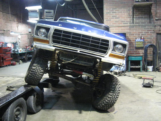 Blue 1978 Ford Bronco with lifted suspension on a trailer in a garage