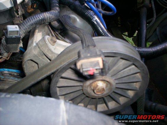 Close-up of a car's engine pulley with a belt around it. There's a connector plugged into the pulley
