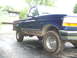 1996 Ford Bronco - A blue Ford F-150 pickup truck is parked on a wet driveway in front of a house.