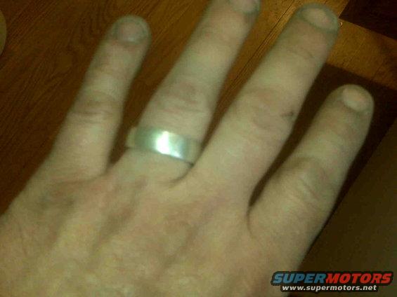 Silver band ring on a person's left hand, with "SUPERMOTORS www.supermotors.net" visible in the lower right corner