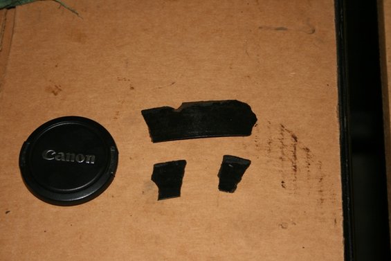 Canon lens cap next to torn black rubber fragments on a brown surface