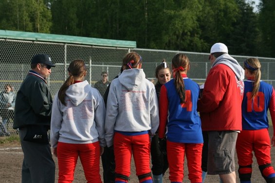 Softball team huddle with coaches and players on field
