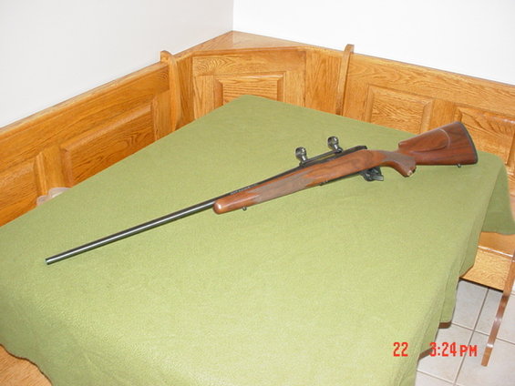 Bolt-action rifle with wooden stock and scope mounts on a green cloth