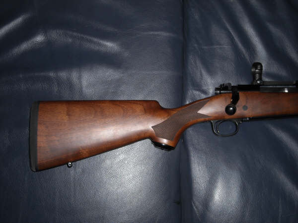 Wooden stock and metal action of a bolt-action rifle on a dark blue surface