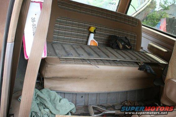 Back seat and cargo area of an old SUV, with a spray bottle on the seat and a shovel on the floor