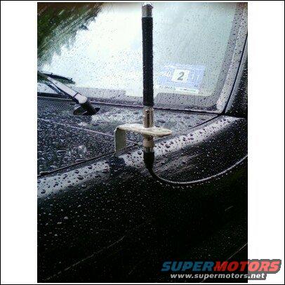 Car antenna mounted on a wet black hood. A sticker with the number 2 is visible on the windshield