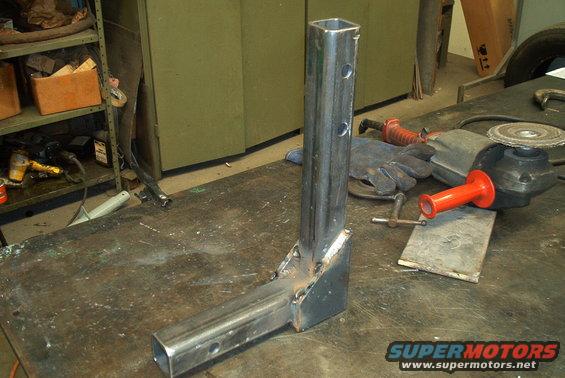 welded metal hitch receiver part on workbench with grinder and gloves