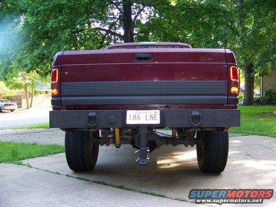 Rear view of a maroon Dodge Ram pickup truck with a custom bumper and trailer hitch. License plate reads 186 LNE