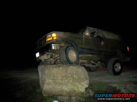 1996 Ford Bronco with front tire on a large rock at night