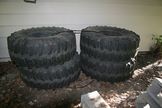 four large off-road tires stacked in pairs outside a building