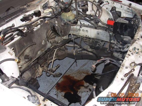 engine bay with brake fluid and oil leaks on the floor, wires and hoses visible