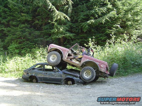 1971 Ford Bronco on top of a crushed sedan, off-road