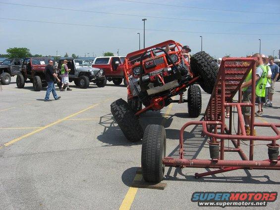 Orange off-road buggy tilted on its side, with other off-road vehicles in background