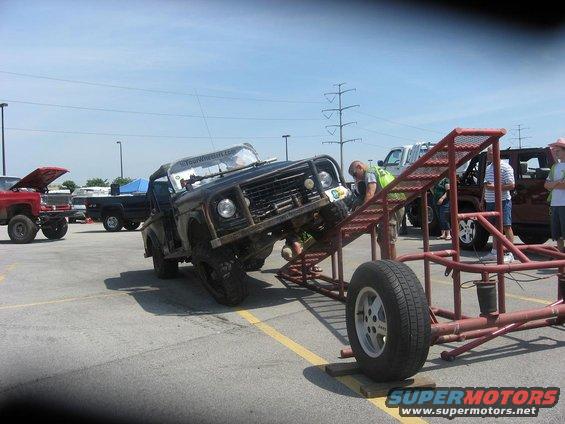 Off-road vehicle attempting an obstacle course, with other trucks parked nearby