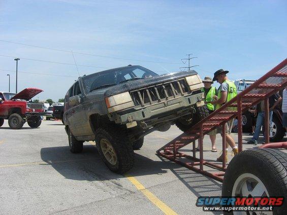 Jeep Grand Cherokee on a ramp with people around. Another lifted truck is in the background