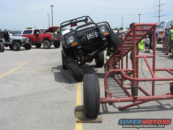 Black off-road vehicle on obstacle course, front-right wheel elevated