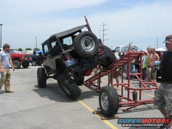 Jeep Wrangler on a ramp with people watching. Red truck in background