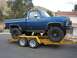 1979 Chevrolet C/K Pickup - A lifted blue pickup truck is loaded onto a yellow trailer, ready for transport.