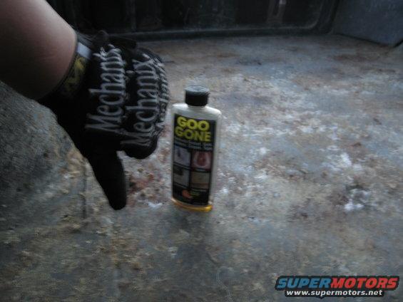 Goo Gone bottle on dirty vehicle floor, hand in Mechanix glove pointing