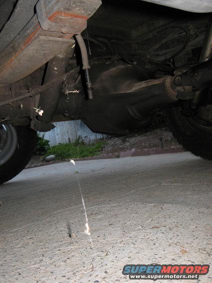 Underside of a vehicle showing the rear axle, leaf springs, and driveshaft. A tire is visible on the left
