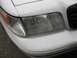 2000 Ford Crown Victoria - The front passenger side headlight and turn signal assembly of a white vehicle are visible.