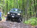 1991 Ford Bronco - This modified Ford Bronco navigates a challenging rocky path through a dense forest.