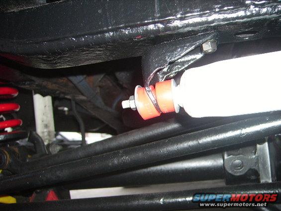 Underbody view of a red suspension bushing and white shock absorber