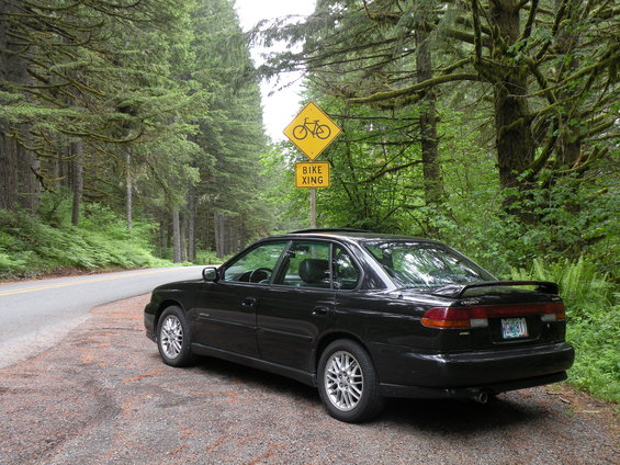 Black sedan parked on a gravel shoulder next to a road with a bike crossing sign