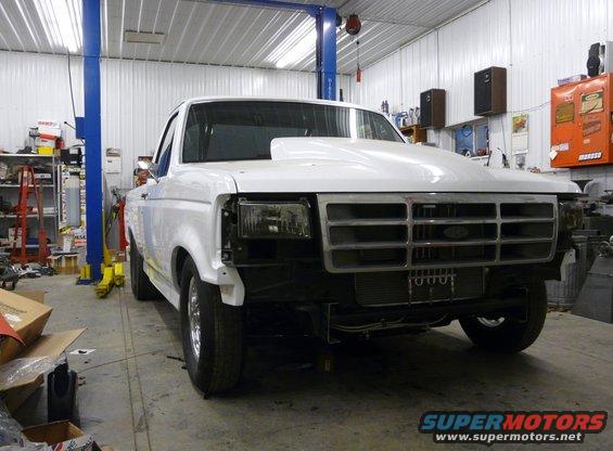 White pickup truck with a large hood scoop, parked in a garage with a lift