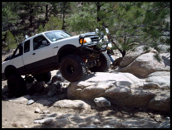 White 1993 Ford Ranger pickup truck with off-road modifications climbing over large rocks